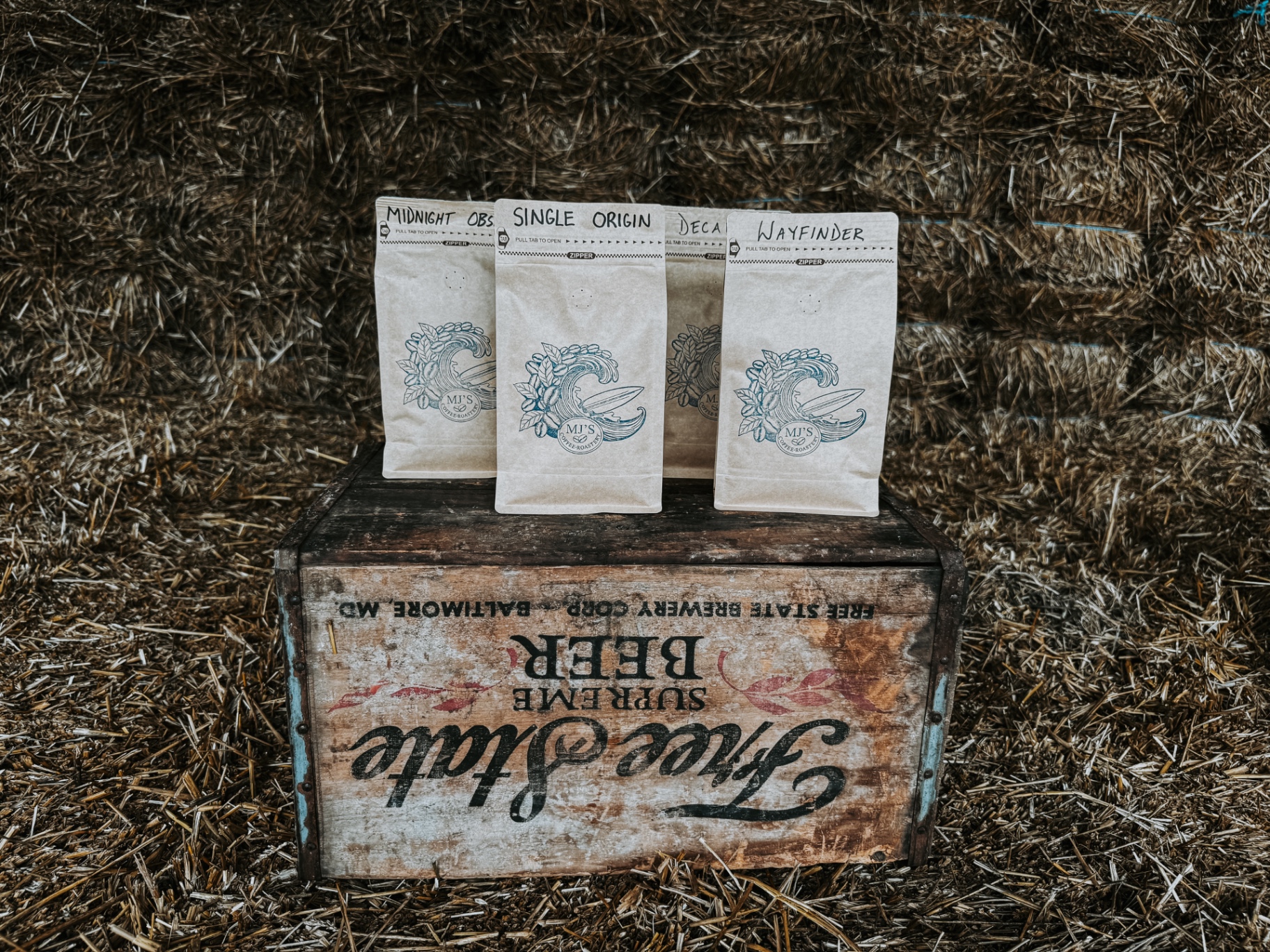 MJ's Coffee Roastery bags — Midnight Obsidian, Single Origin, Decaf, and Wayfinder — on a vintage Free State Brewery crate